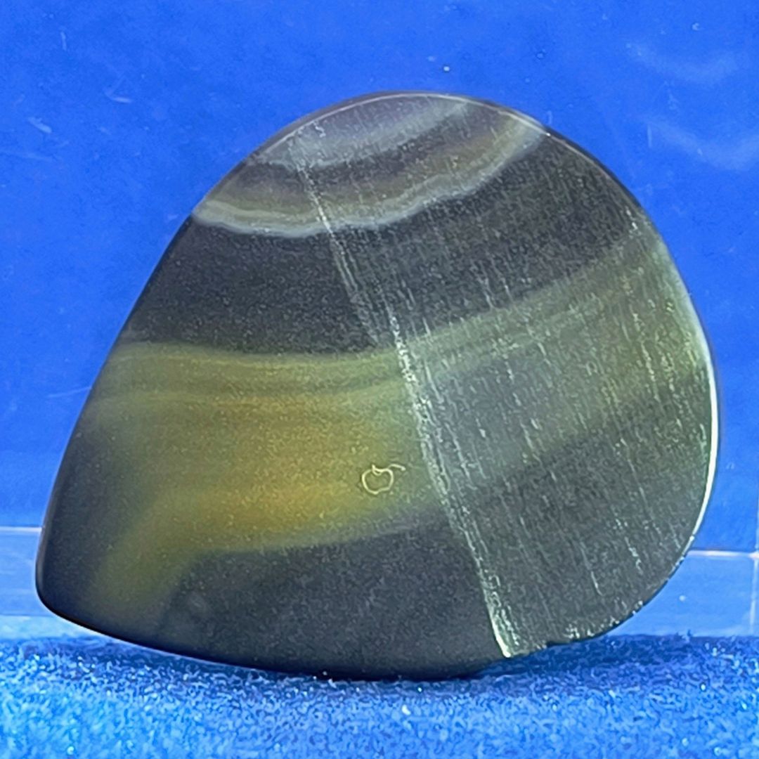 Plettro in pietra di onice nera con striature bianche trasparenti e adesivo con micro granuli di quarzo per ottimizzare il grip e la presa sul codolo del plettro, fotografato con sfondo azzurro.